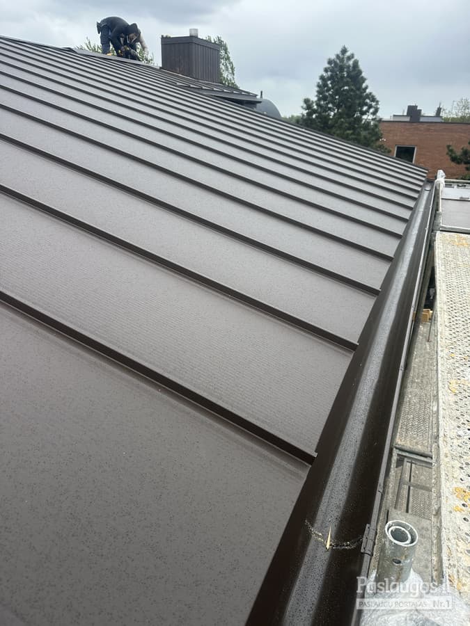 Skardinis stogas su nauju lataku renovacijos metu – darbininkas matomas kraige