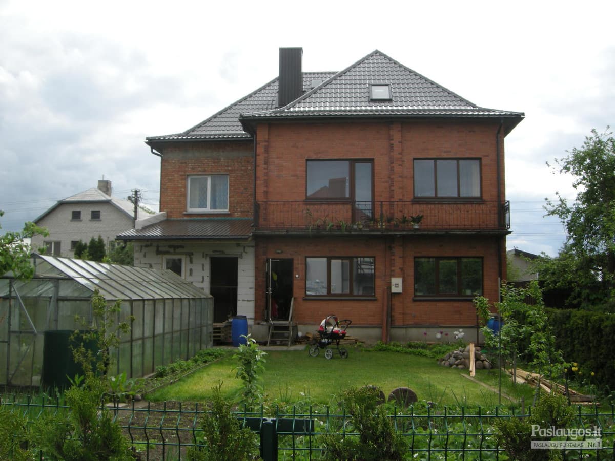 Raudonos plytų namas su pilkais čerpių stogu – sodrus vasaros žalumas